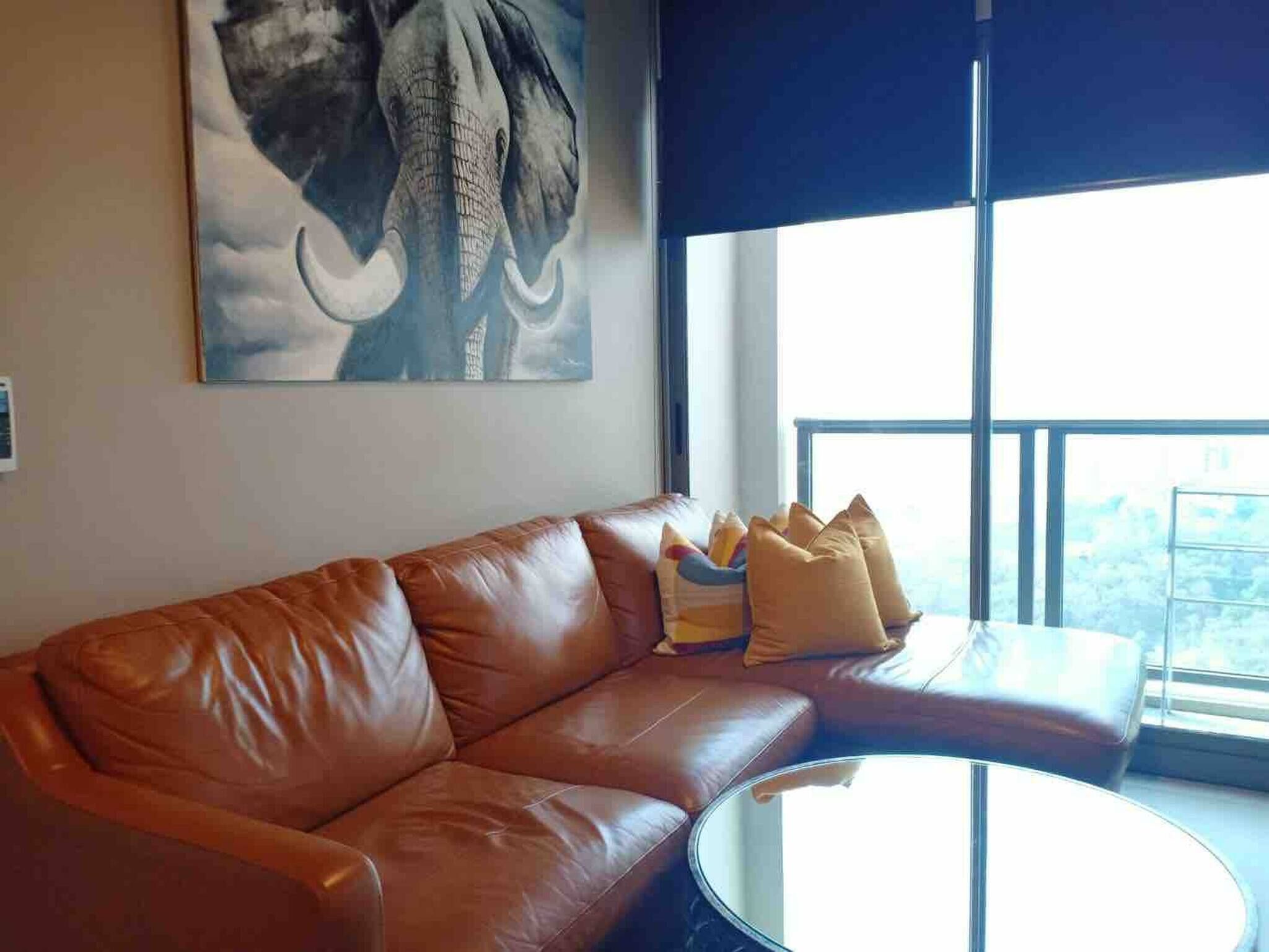 A modern living room with a leather sofa, a round coffee table, and a large window offering a city view.
