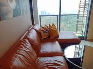 A modern living room with a leather sofa, a glass coffee table, and a large window with a city view.