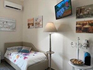 Relax in a cozy bedroom with a neatly made bed, floor lamp, and wall-mounted TV.