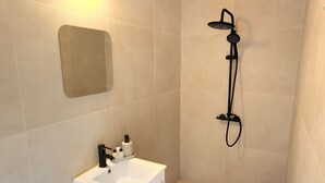 Ein Badezimmer mit einem weißen Waschbecken, einem Spiegel und einer Dusche mit Duschbrause.