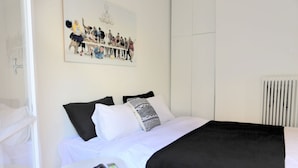Ein Schlafzimmer mit einem Bett, einem kleinen runden Tisch mit einer Sonnenbrille und einem Telefon sowie einem Wandbild über dem Bett.