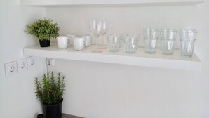 Ein Küchenregal mit weißen Tellern, Tassen und Gläsern, sowie zwei Blumentöpfen.