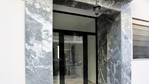 A modern building entrance with a glass door, marble walls, and a small step leading up to the door. - Junior Unicorn Suite (Athens)