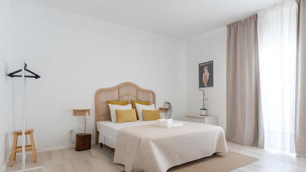A neatly arranged bedroom with a bed, a bedside table, a hanging coat rack, and a window with curtains. - Galagana Charm House (Golega)