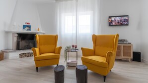 A modern living room with two yellow armchairs, a fireplace, a television, and a small table with decorative items. - Galagana Charm House (Golega)
