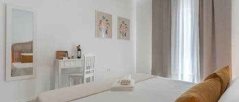 A hotel room with a bed, a desk, a chair, a mirror, and artwork on the wall.