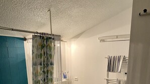 Une salle de bain avec une baignoire, un rideau de douche orné d’un motif de cactus, un lavabo, un porte-serviettes et une poubelle.