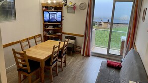 Une pièce chaleureuse avec une table et des chaises en bois, un téléviseur posé sur une étagère, un canapé et un balcon avec vue.