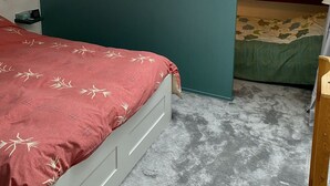 Une chambre avec une lucarne, un lit recouvert d’une courtepointe rouge et, au fond, un lit superposé.