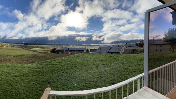 Une vue depuis un balcon donnant sur un paysage verdoyant, avec des maisons visibles au loin sous un ciel partiellement nuageux.