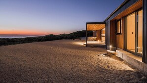 Une maison moderne dotée d’un vaste espace extérieur et offrant une vue sur l’océan au crépuscule.