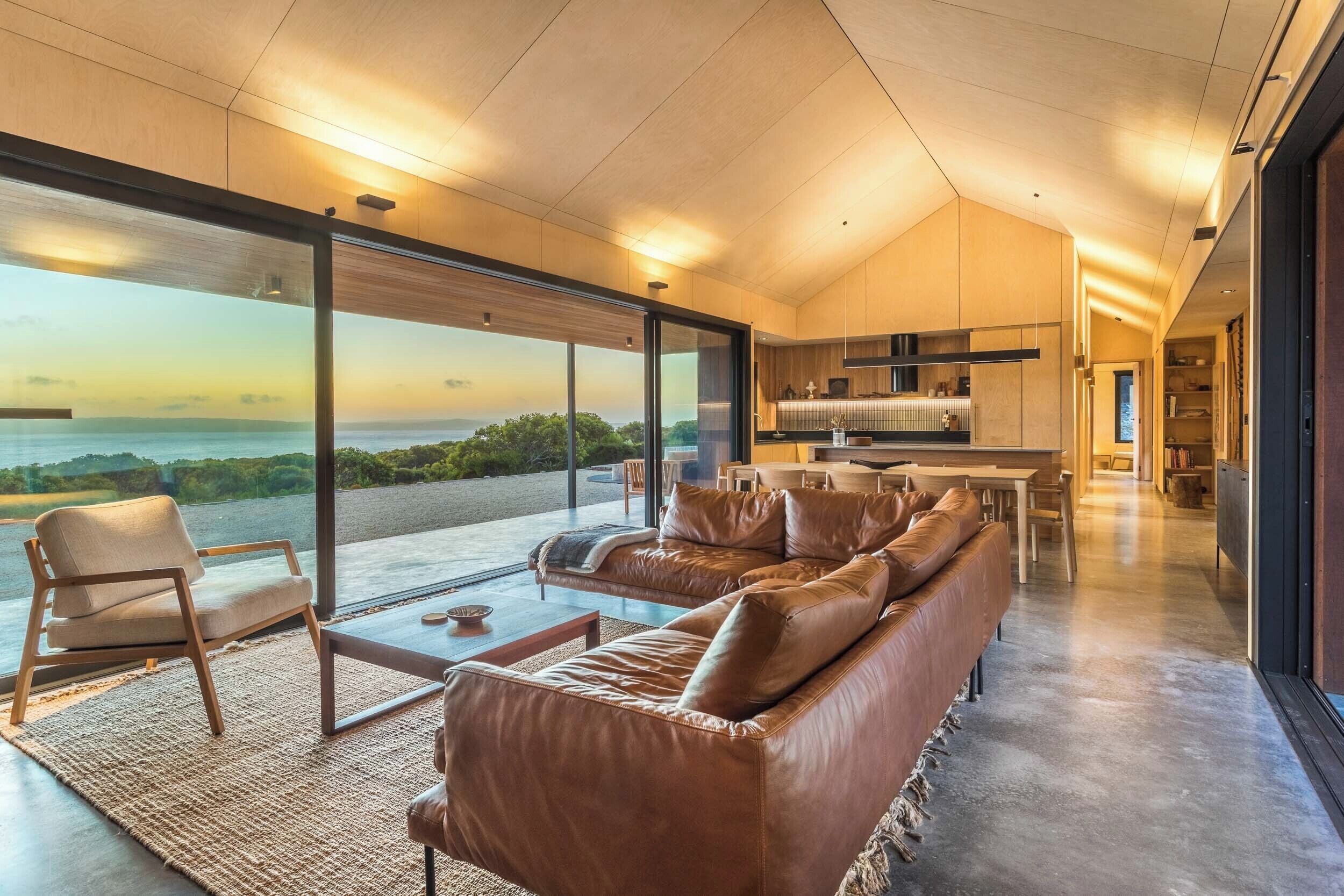 A modern living room with a large sofa, a coffee table, and a view of the sea.