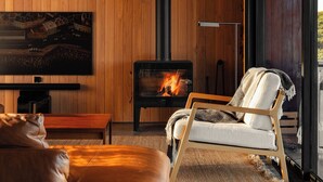 Un salon moderne doté d’une cheminée, de murs recouverts de panneaux de bois, d’un grand téléviseur, d’un canapé en cuir et offrant une vue sur l’extérieur grâce à de grandes portes vitrées.