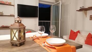 Ein Essbereich mit einem Holztisch, gedeckt für zwei Personen, einer Laterne und einer Couch mit roten Kissen.