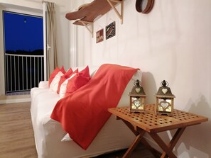 Une chambre avec un lit, une couverture rouge, deux lanternes fixées au mur, une étagère en bois et une vue sur le ciel nocturne.