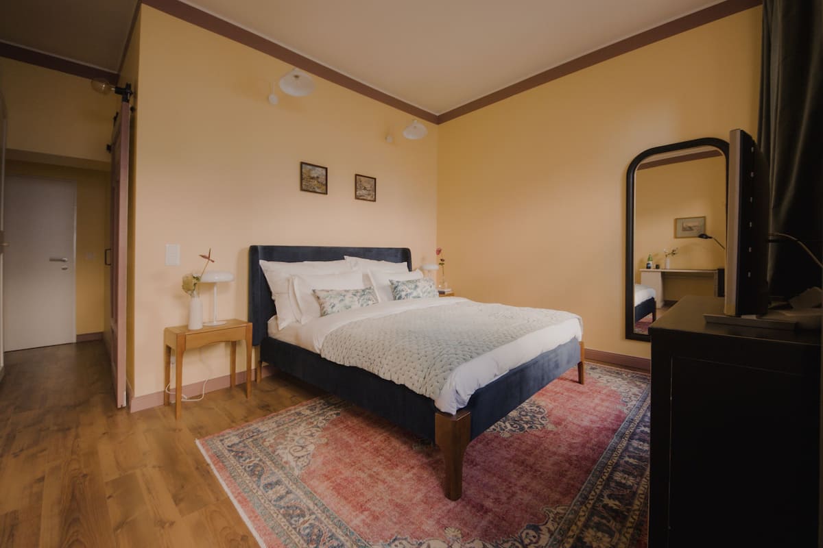 Un dormitorio con cama, mesita de noche, lámpara y espejo.