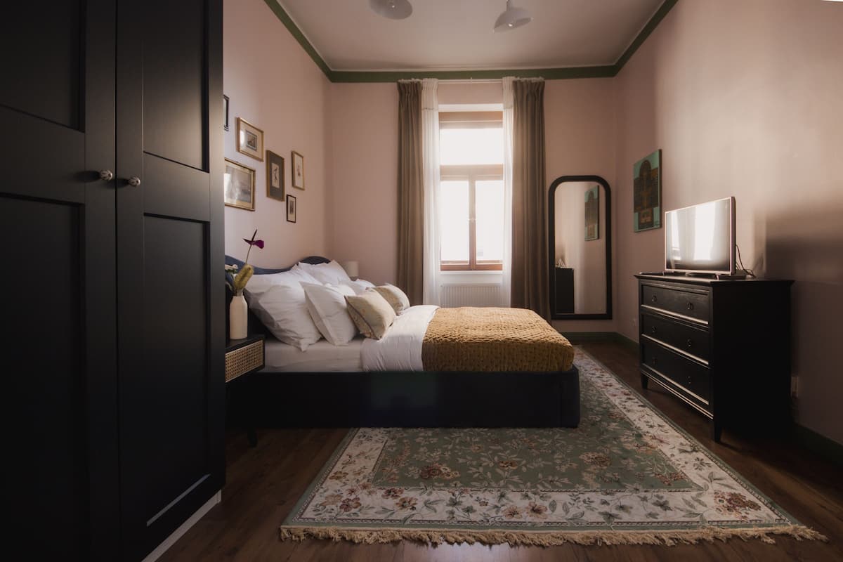 Un dormitorio con cama, cómoda, espejo y televisor sobre un soporte.