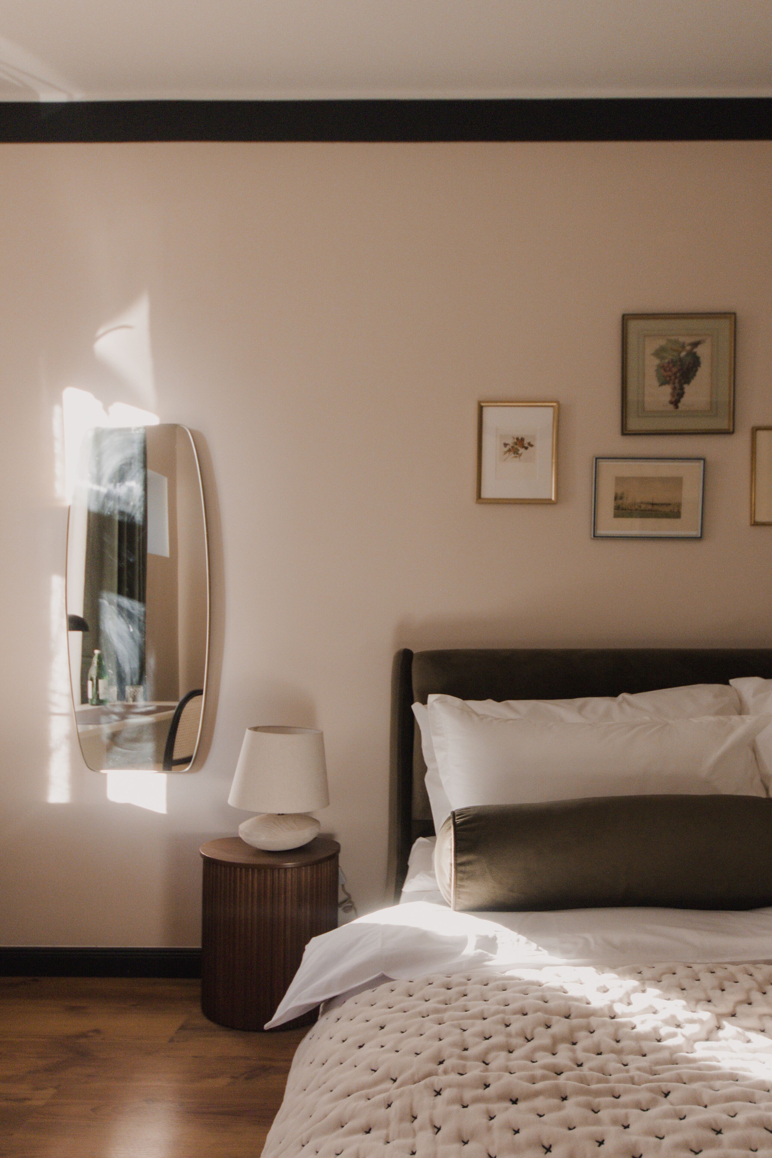 Ein Schlafzimmer mit einem Bett, einem Nachttisch mit Lampe, einem Spiegel und gerahmten Bildern an der Wand.