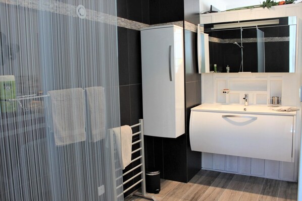 Un baño moderno con cabina de ducha de vidrio, un lavabo blanco y un espejo grande sobre el lavabo.
