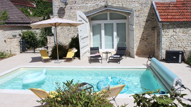 Un bâtiment en pierre doté d’une piscine, d’un espace extérieur aménagé et d’une porte avec des panneaux de verre.