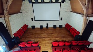 Un petit théâtre à l’ambiance chaleureuse, doté d’un plancher en bois, de sièges rouges et d’un grand écran blanc.