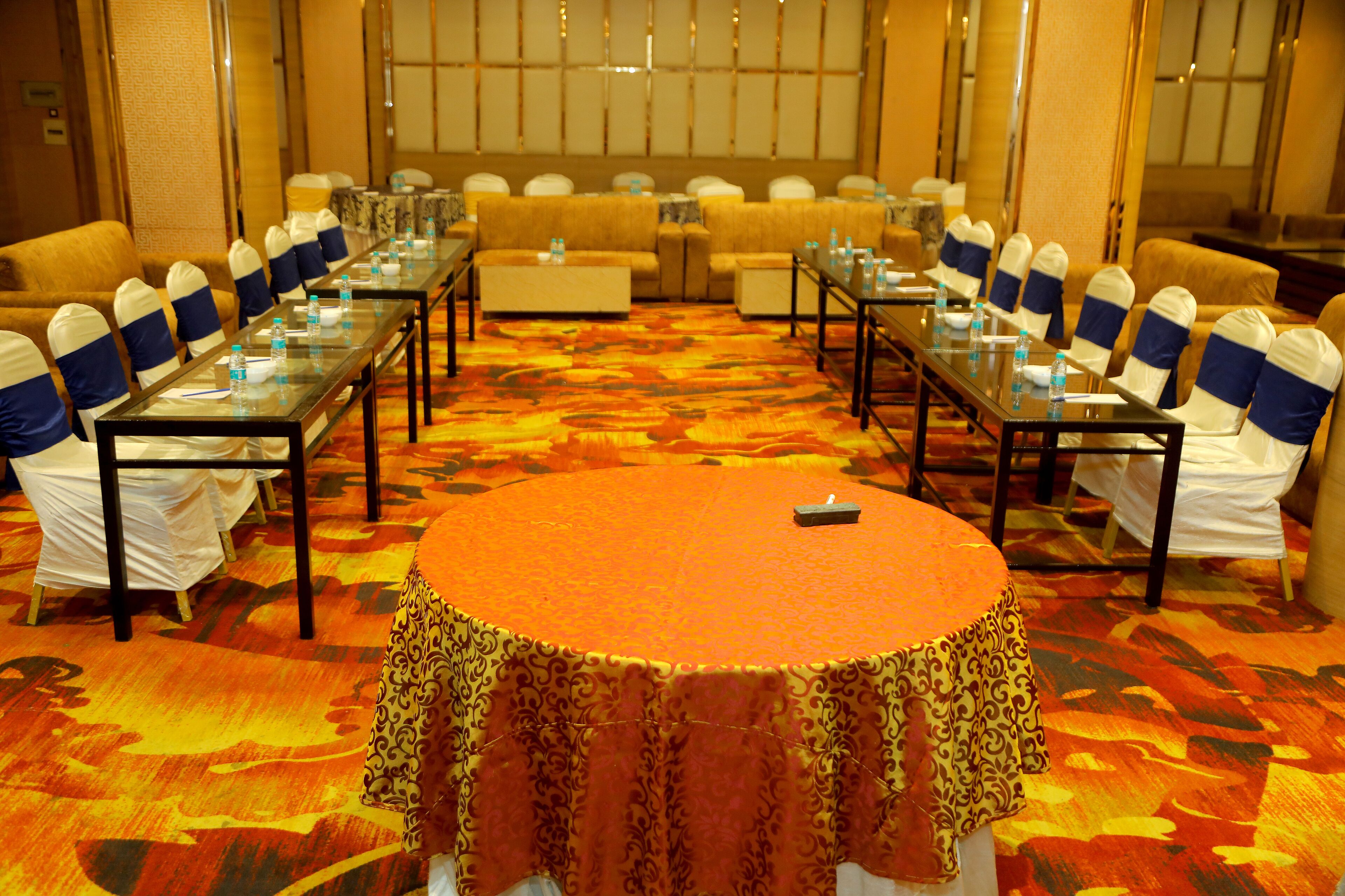 A conference room with a large oval table, multiple smaller tables, and rows of chairs with blue sashes.