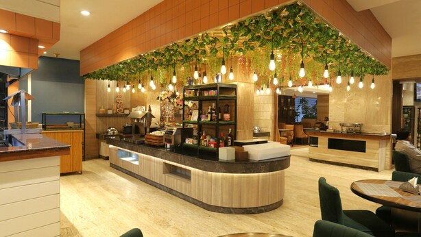 Un hall d’hôtel moderne avec un comptoir d’accueil incurvé, un espace salon et une grande installation végétale au-dessus du comptoir.