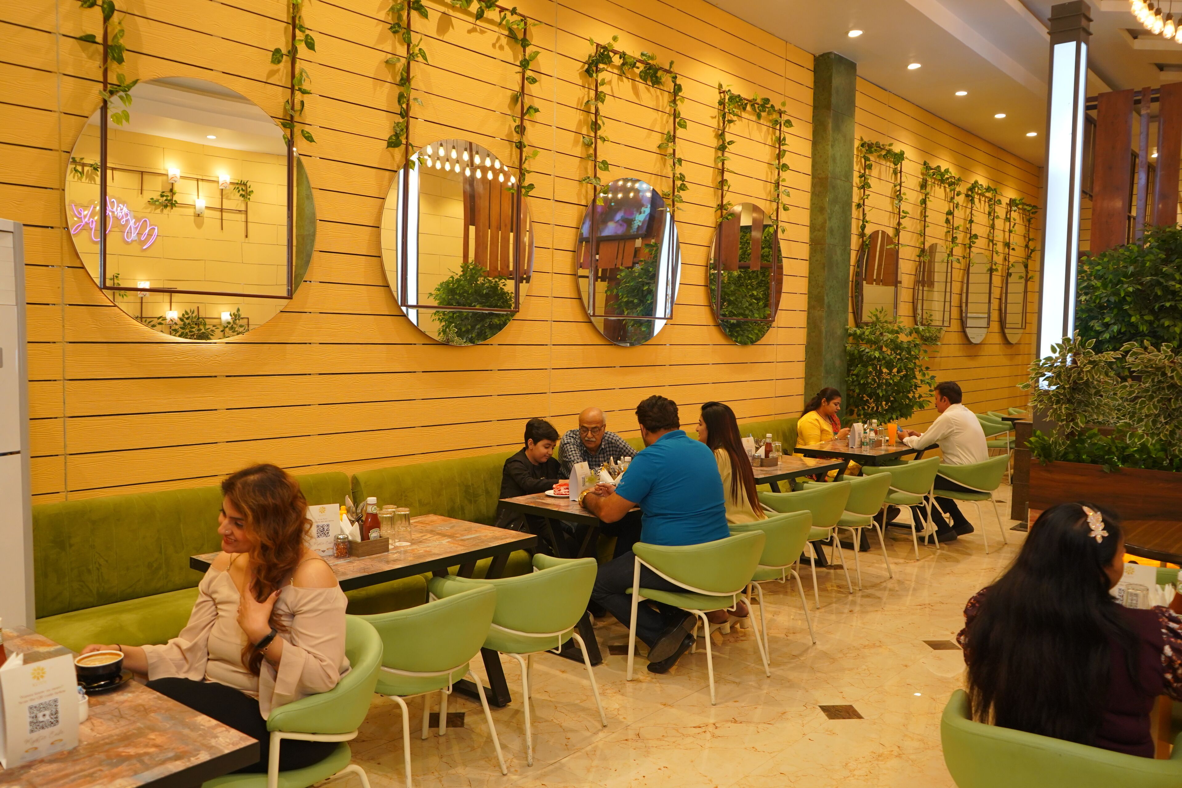 Un restaurante con espejos redondos en la pared, sillas verdes y mesas con comensales.