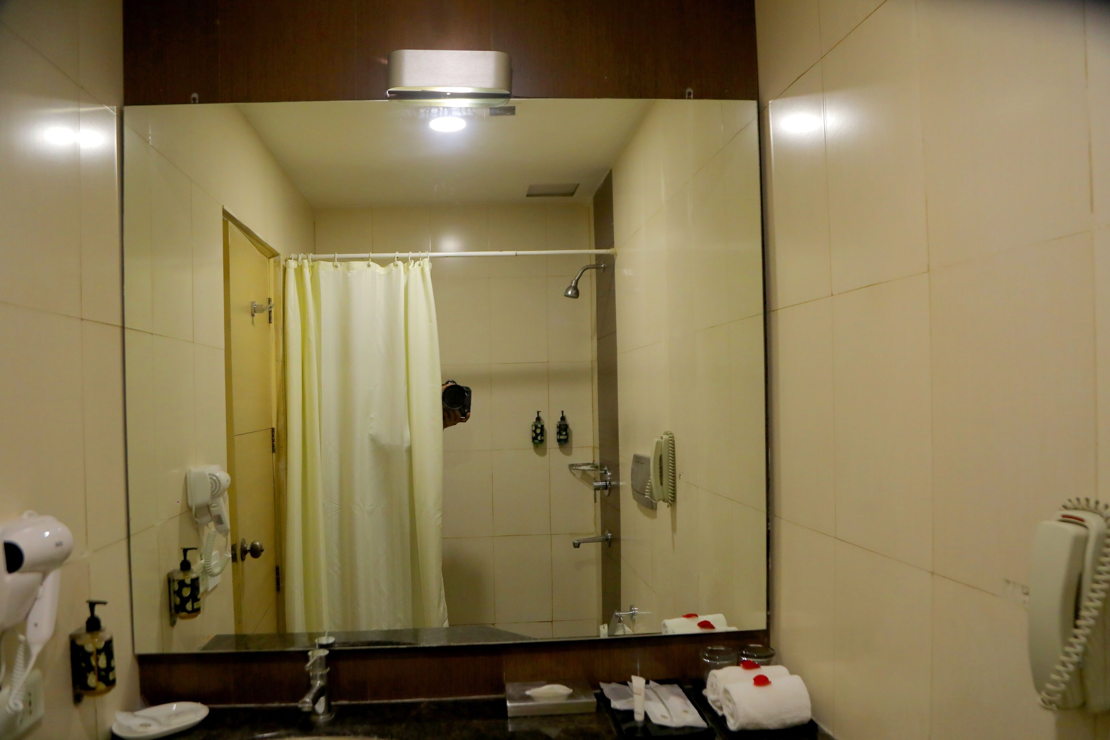 A bathroom with a large mirror, a shower, a hairdryer, a towel, and a phone.