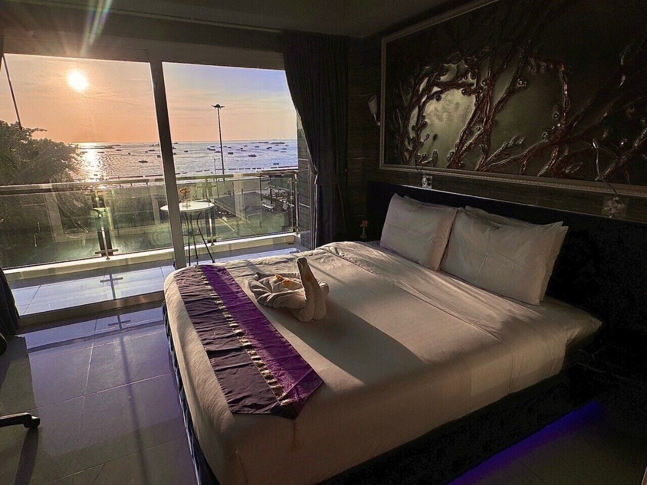 A hotel room with a large bed, a view of the ocean through a balcony, and a decorative wall piece.