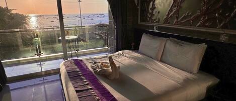 A hotel room with a large bed, a view of the ocean through a balcony, and a decorative wall piece.