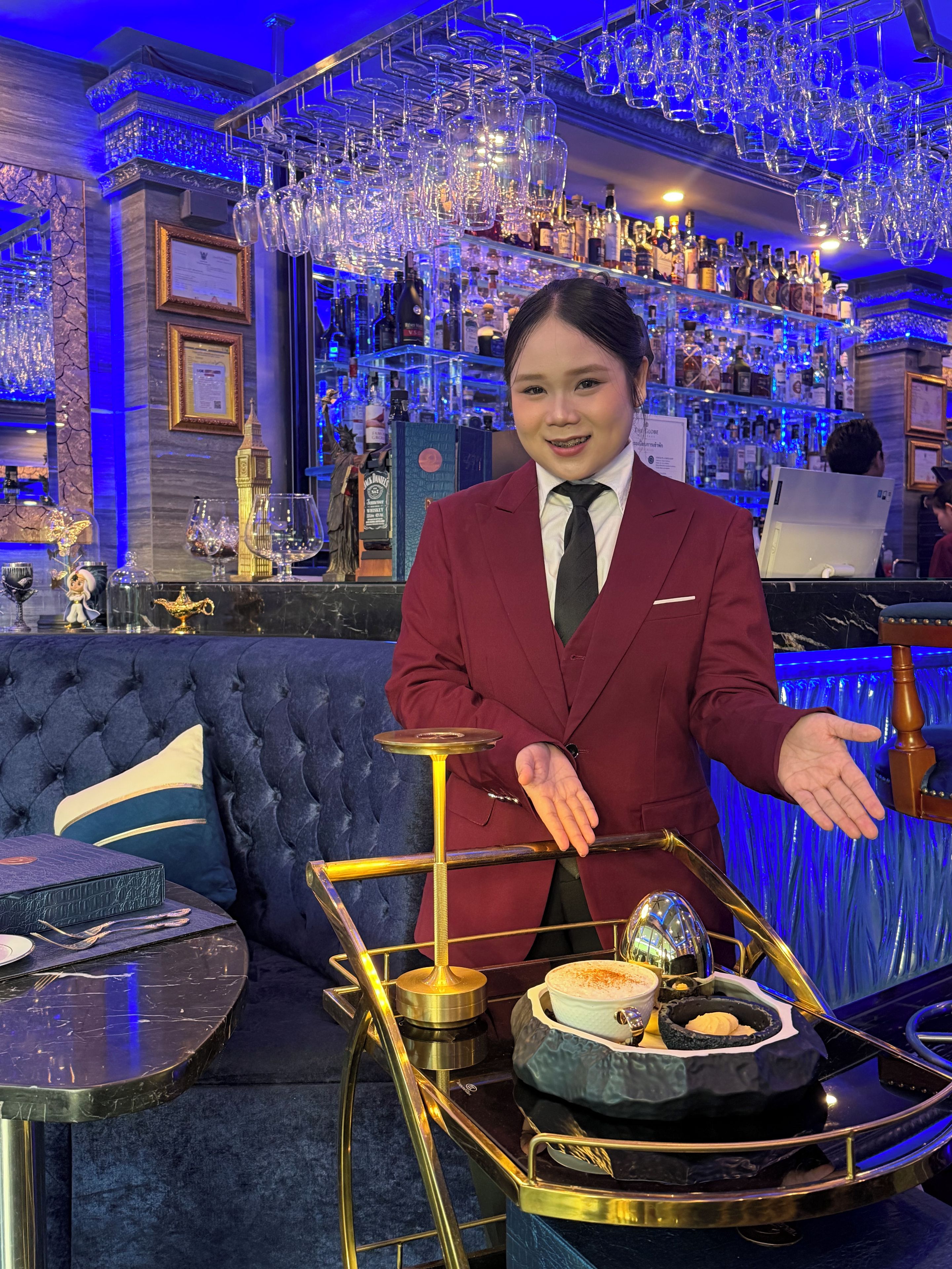 A bar area with a bartender, a bar counter, and a variety of bottles and glasses.