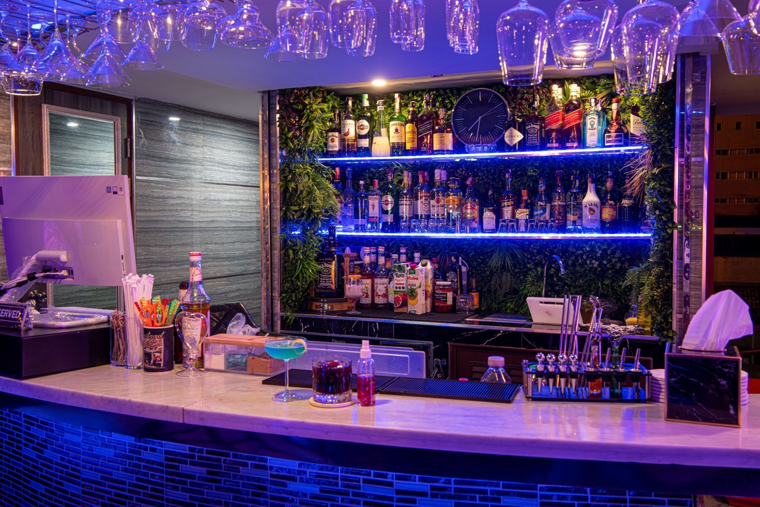 A bar area with shelves of liquor bottles, a clock, and bar tools.