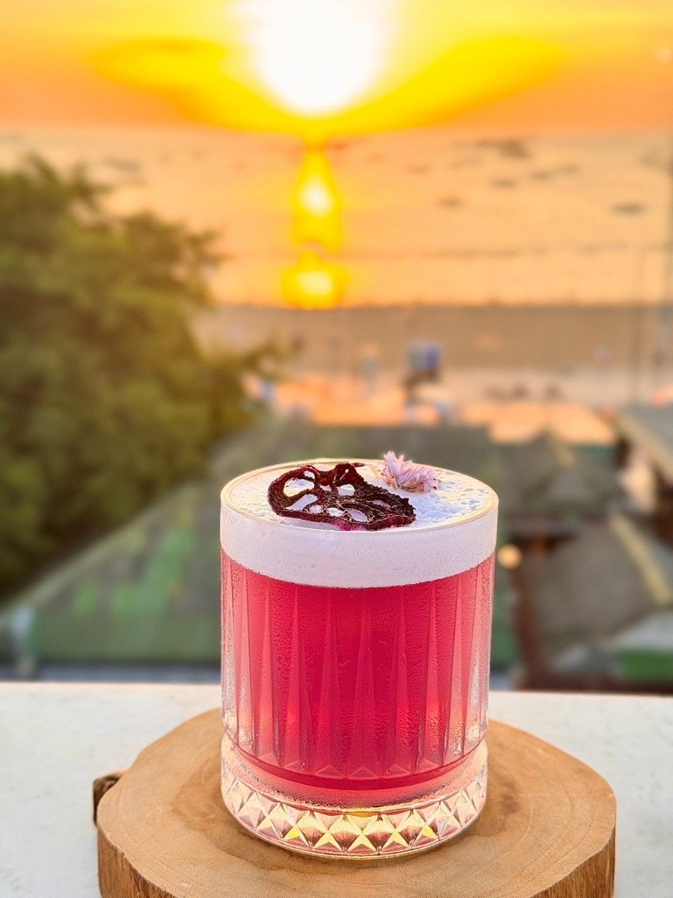 A clear glass with a red beverage, possibly a cocktail, on a wooden coaster.