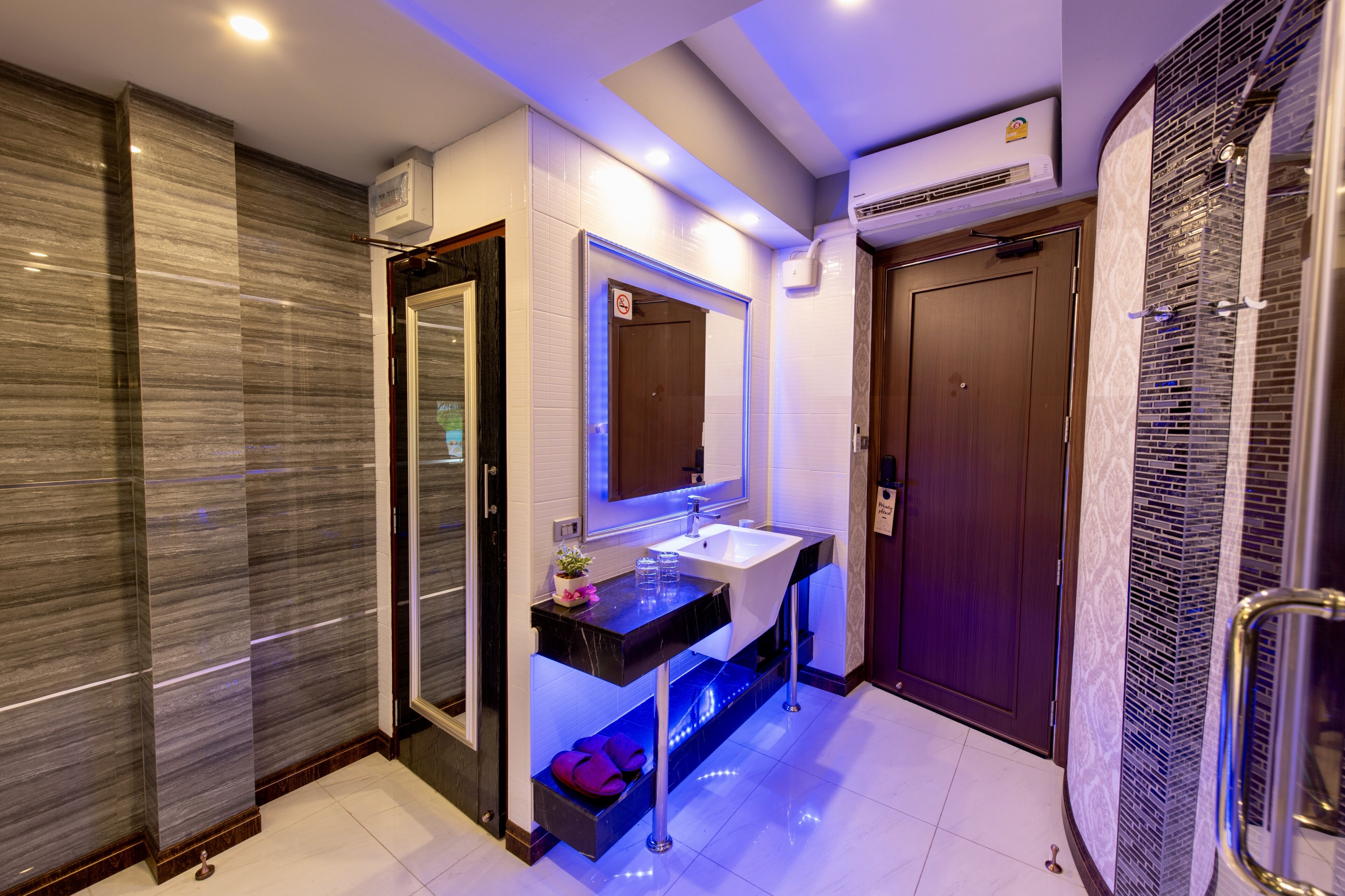 A modern bathroom with a marble wall, a sink with a mirror, and a shower area.