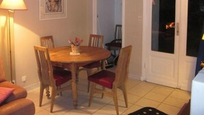 A dining area with a wooden table and four chairs, a sofa with a cushion, a lamp, and a door with a view of the outside. - Touquettoise 'Romeo (Paris)