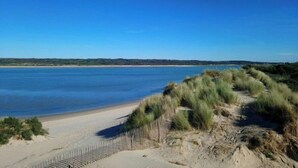 A beach with a sandy path leading to the water, surrounded by grassy dunes. - Touquettoise 'Romeo (Paris)