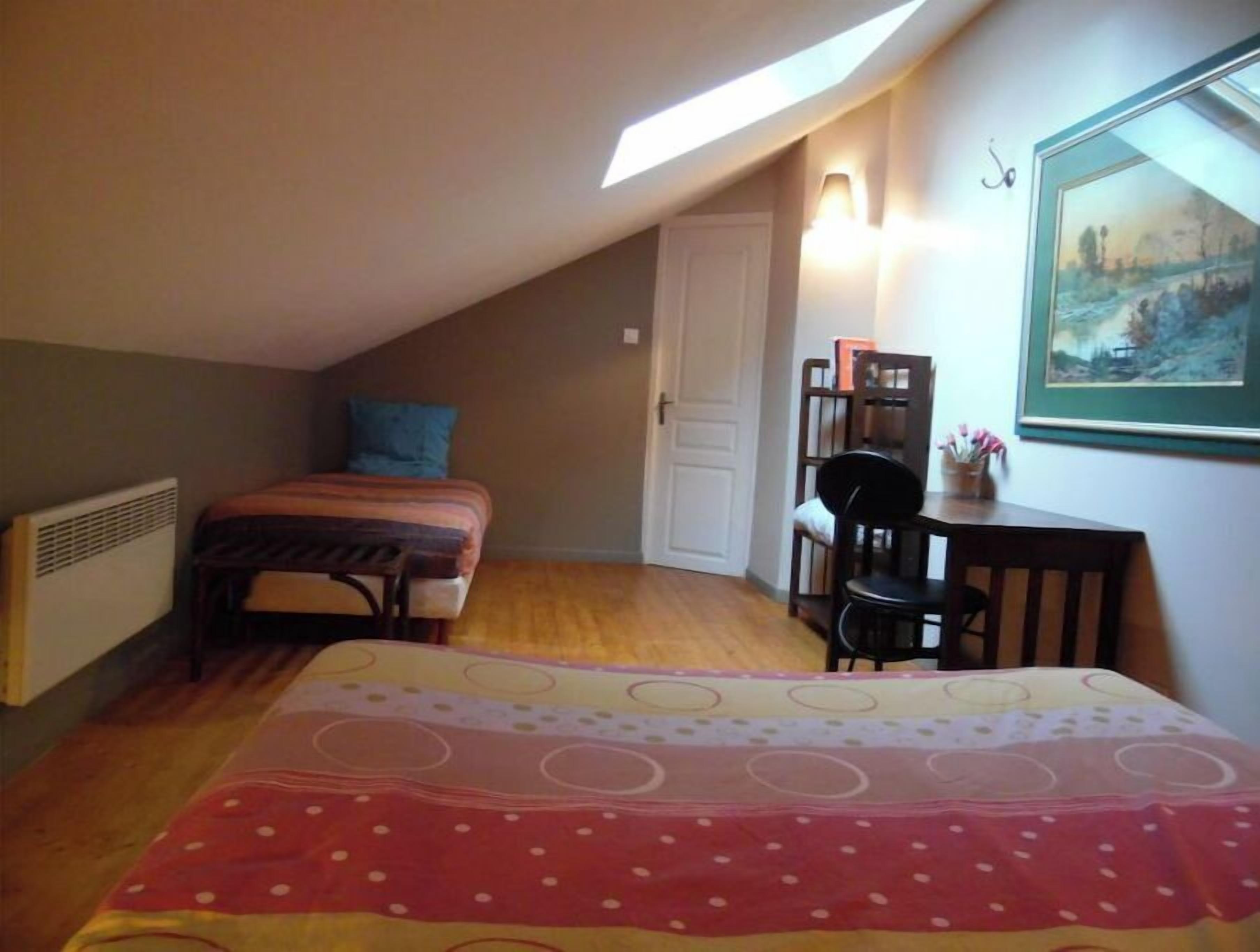 Un dormitorio con techo inclinado, una cama con colcha a rayas, un escritorio con silla y un cuadro en la pared.