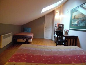 A bedroom with a sloped ceiling, a bed with a striped blanket, a desk with a chair, and a painting on the wall. - Touquettoise 'Romeo (Paris)