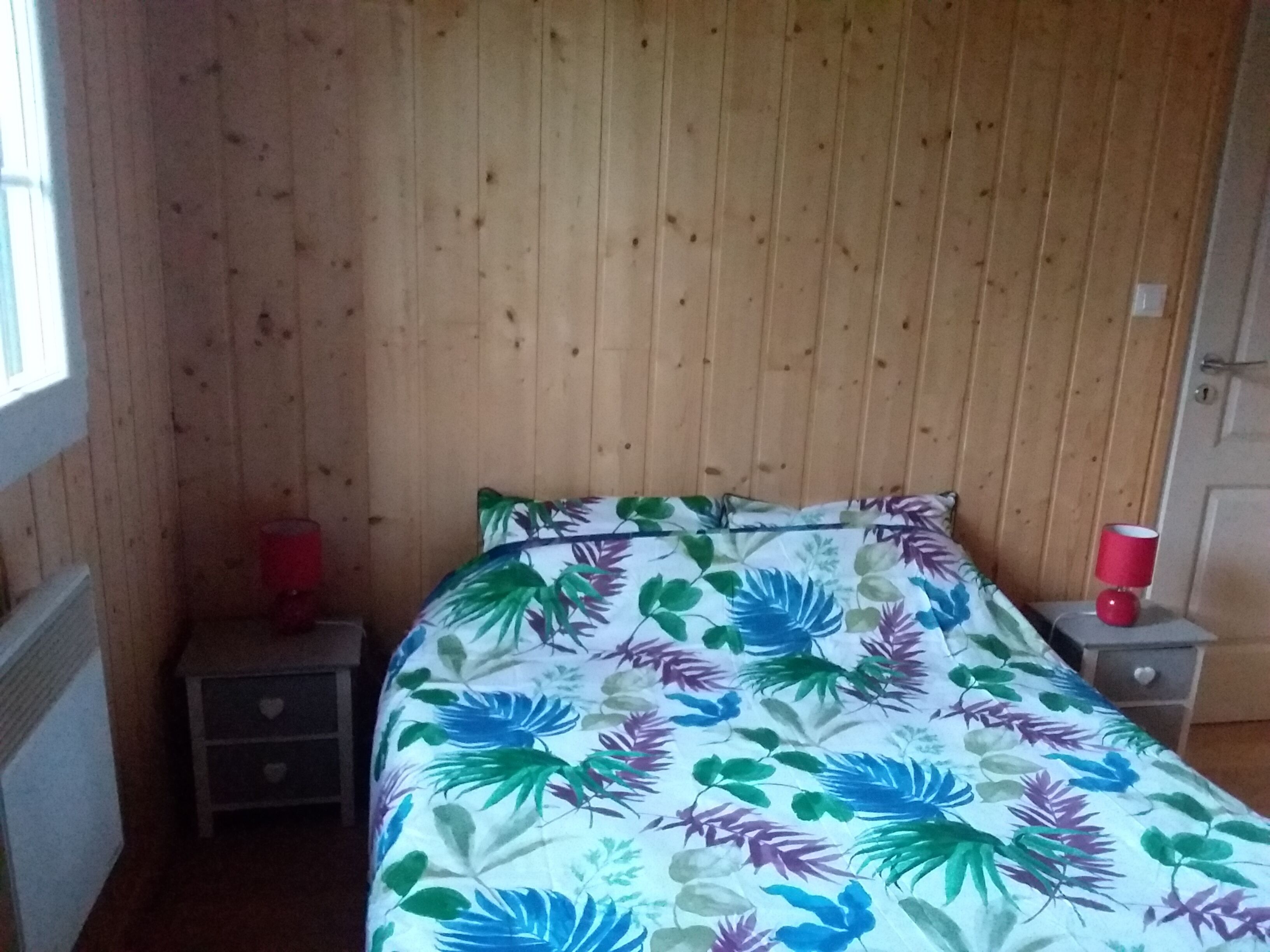 A room with a bed, a nightstand, a red lamp, and a wooden wall.