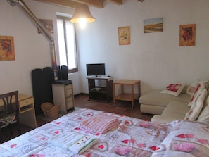 A bedroom with a bed, a desk with a computer, a chair, a sofa, and a window.