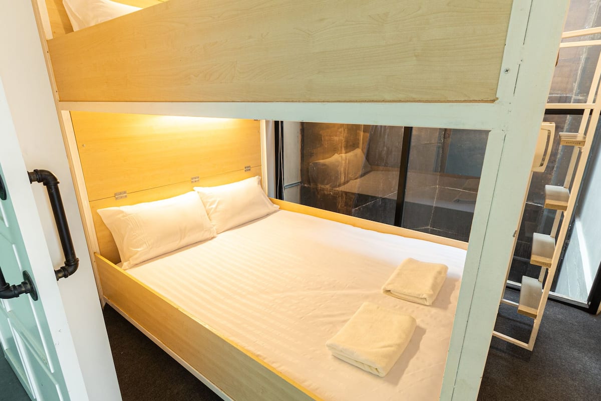 Een stapelbed met een houten hoofdeinde, wit beddengoed en een raam met uitzicht.