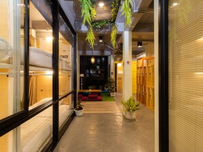 A corridor with bunk beds, a seating area with cushions, and potted plants. - Khaosan Social Capsule Bangkok - Adult Only - Hostel (Bangkok)