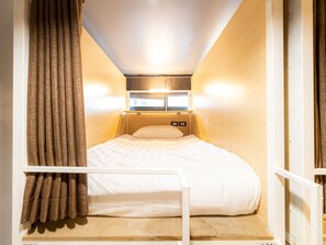 Een kleine kamer met een enkel bed, een raam, gordijnen en een hoofdbord.