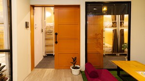 Een kamer met een houten deur, een kleine potplant, een rode bank en een gele tafel.