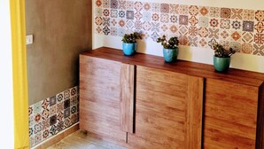 A room with a wooden cabinet, tiled backsplash, and a yellow curtain.