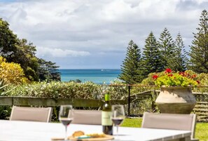 An outdoor dining area with a table set for two, overlooking a coastal view with trees and a body of water.