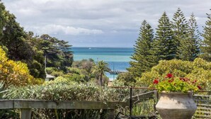 A coastal garden with a view of the sea, a wooden fence, and a large planter with flowers. - Horizon View Retreat by Ready Set Stay - Beach Views (Sorrento)