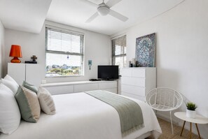 A modern bedroom with a bed, a TV, a desk, and a chair.
