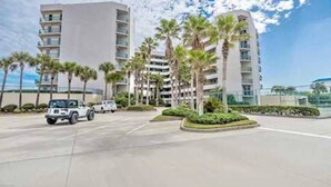 A modern hotel with multiple floors, palm trees, and a parking area with vehicles.